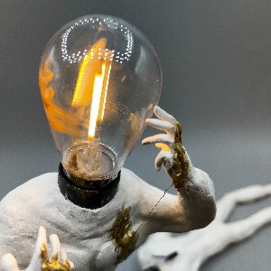 Close up of a sculpted human figure with a lightbulb for a head